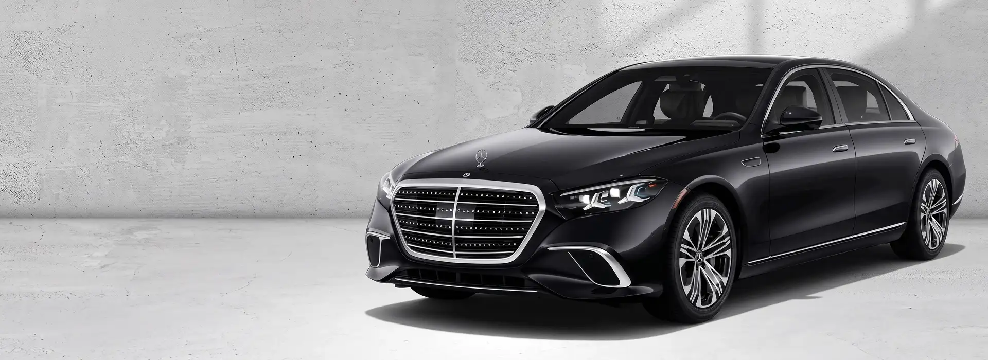 Black 2027 Mercedes-Benz S 580 4MATIC Sedan angled in front of a gray concrete wall
