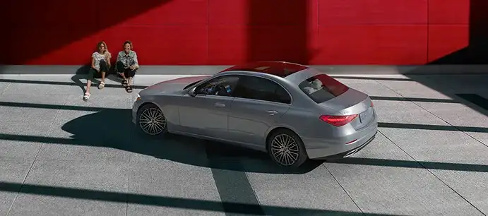 Silver C 300 4MATIC Sedan parked in front of a red wall with two people nearby.