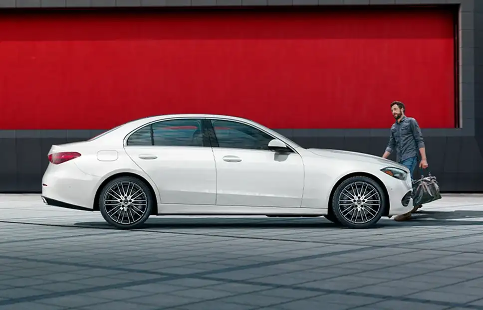 White C 300 4MATIC Sedan in profile beside a red wall.