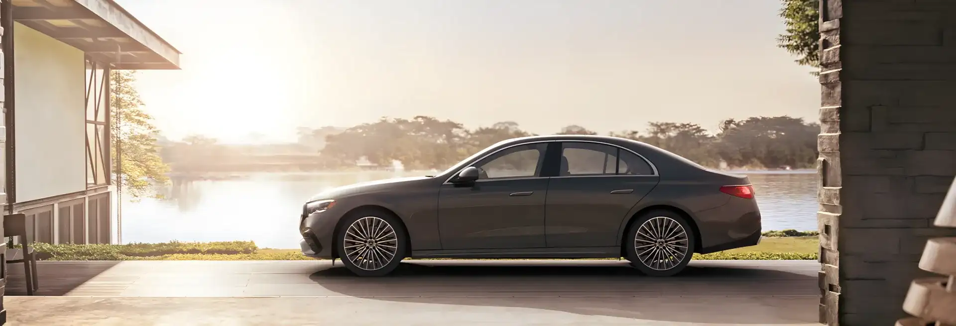 Grey E 350 4MATIC Sedan parked in an open carport overlooking a lake at sunrise.
