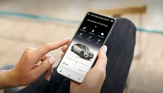 Hand holding a phone showing the Mercedes-Benz app with the vehicle ready to start remotely.
