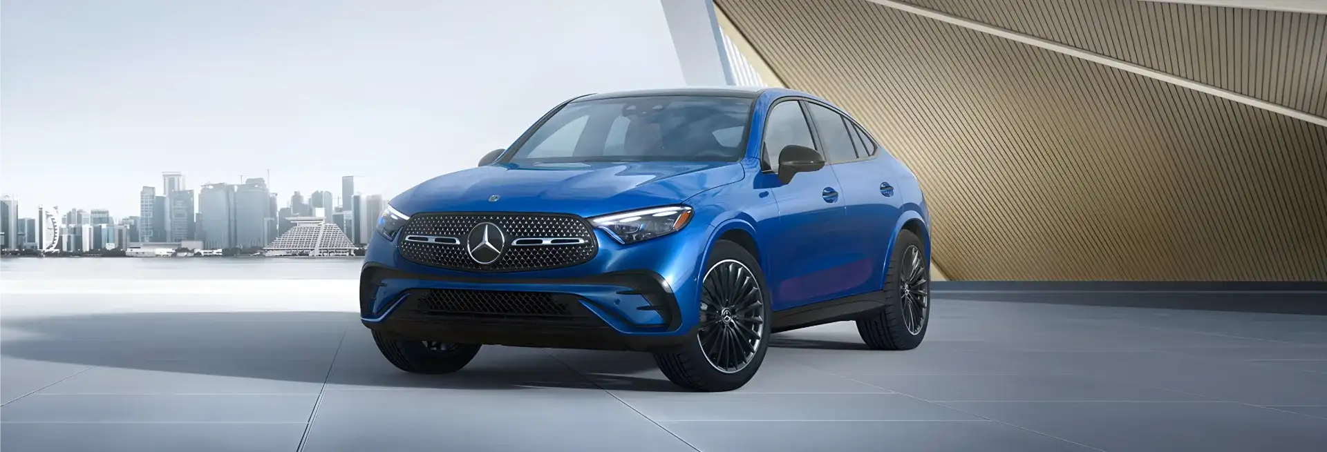 Blue GLC 300 4MATIC Coupe parked in front of a modern building with a city skyline behind.