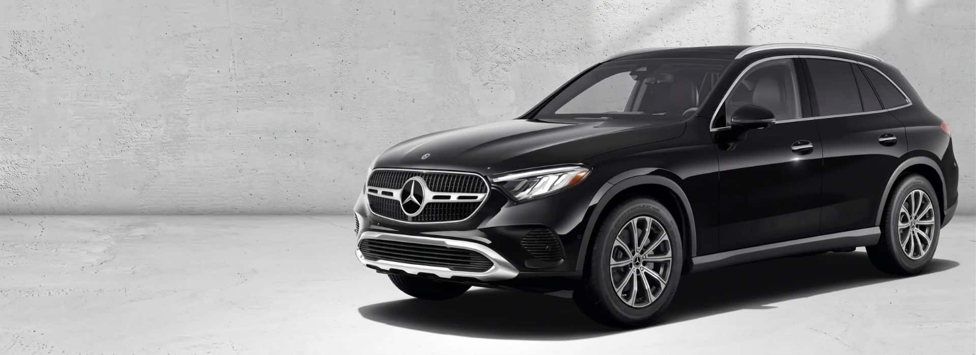 Black 2027 Mercedes-Benz GLC 300 4MATIC&reg; SUV shown from a front three-quarter angle against a pale concrete wall.