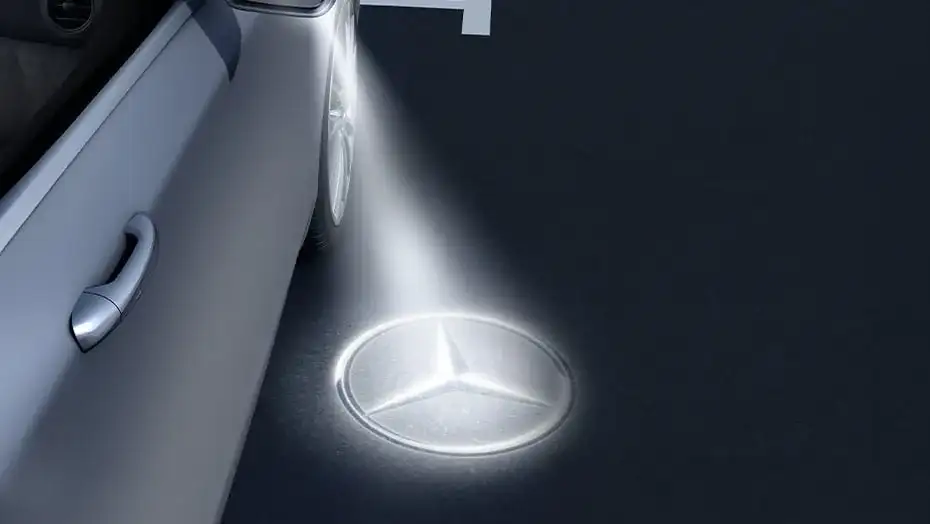 Mercedes-Benz Star projected onto the ground beside the door of a GLC at night.