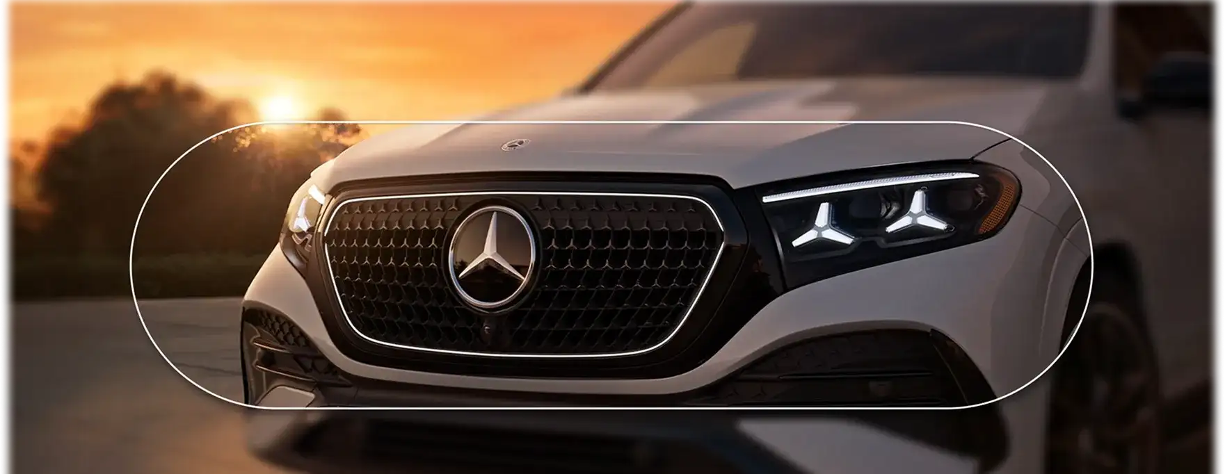 Close front view of a white GLE at sunset with the illuminated Star grille and Star-motif headlamps.