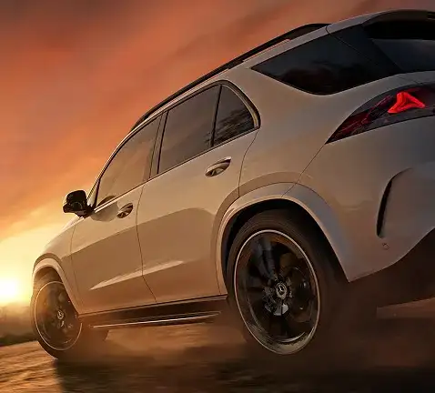 White GLE 450 4MATIC SUV kicking up dust, seen from a low rear three-quarter angle at sunset.