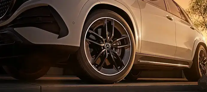 Low view of the AMG wheel and front fender of a white GLE at sunset.