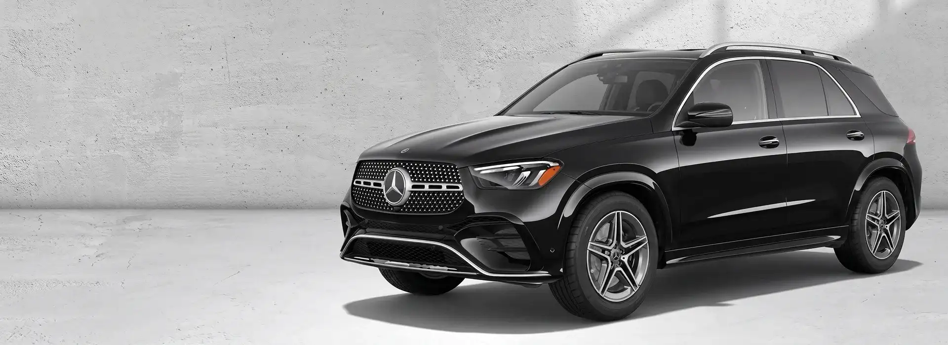 Black 2027 Mercedes-Benz GLE 450 4MATIC SUV shown from a front three-quarter angle against a pale concrete wall.