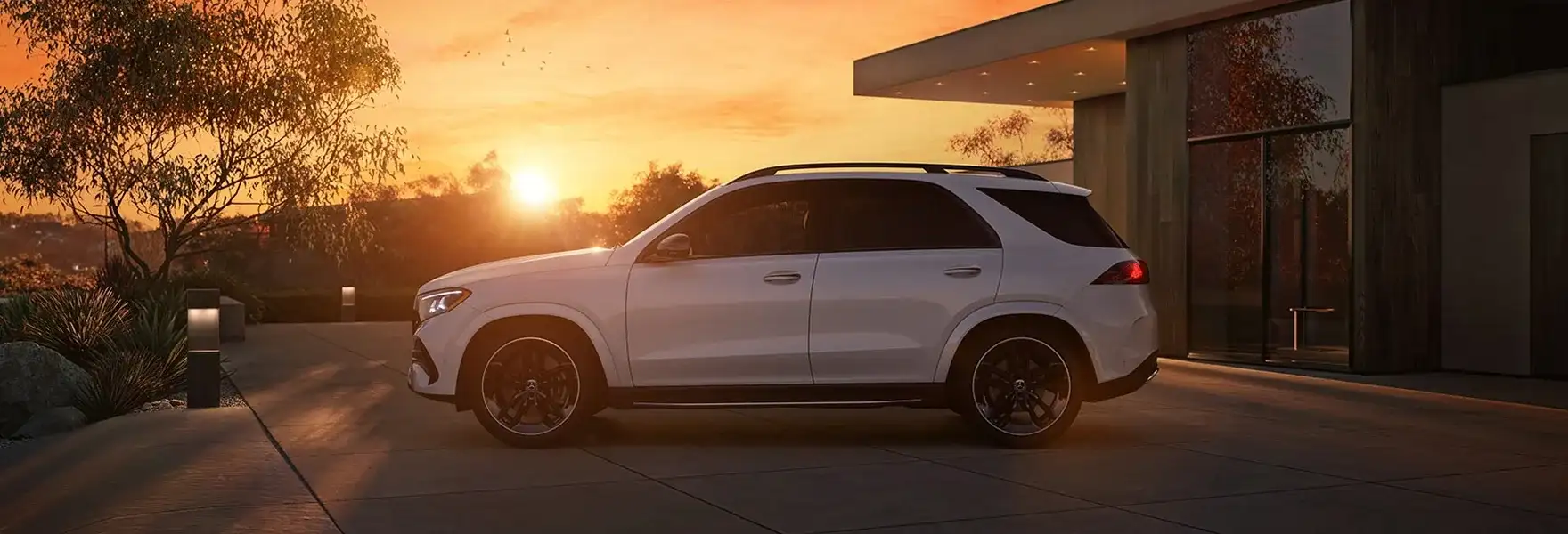 White GLE 450 4MATIC SUV in profile on a driveway at sunset.