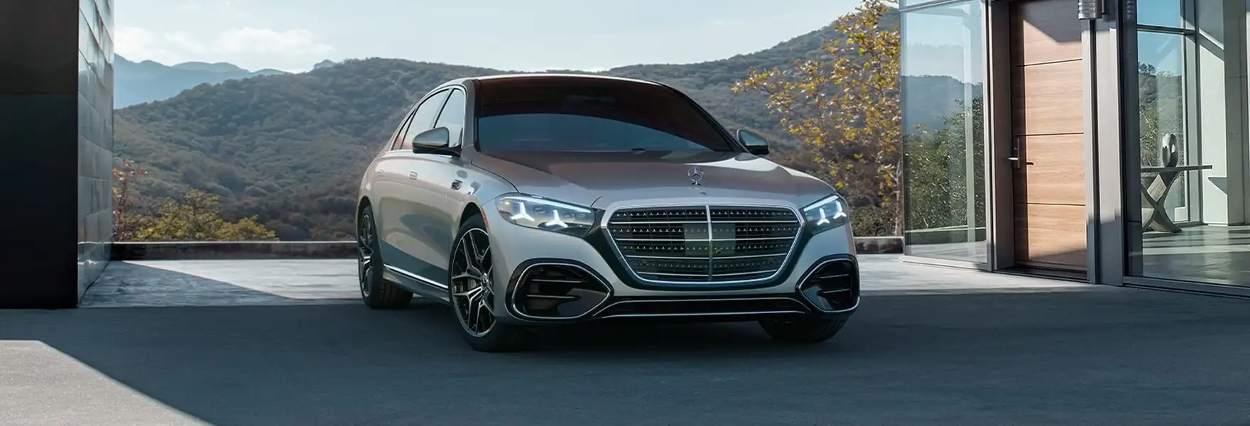 Silver Mercedes-Benz S-Class parked outside a modern glass home in the mountains
