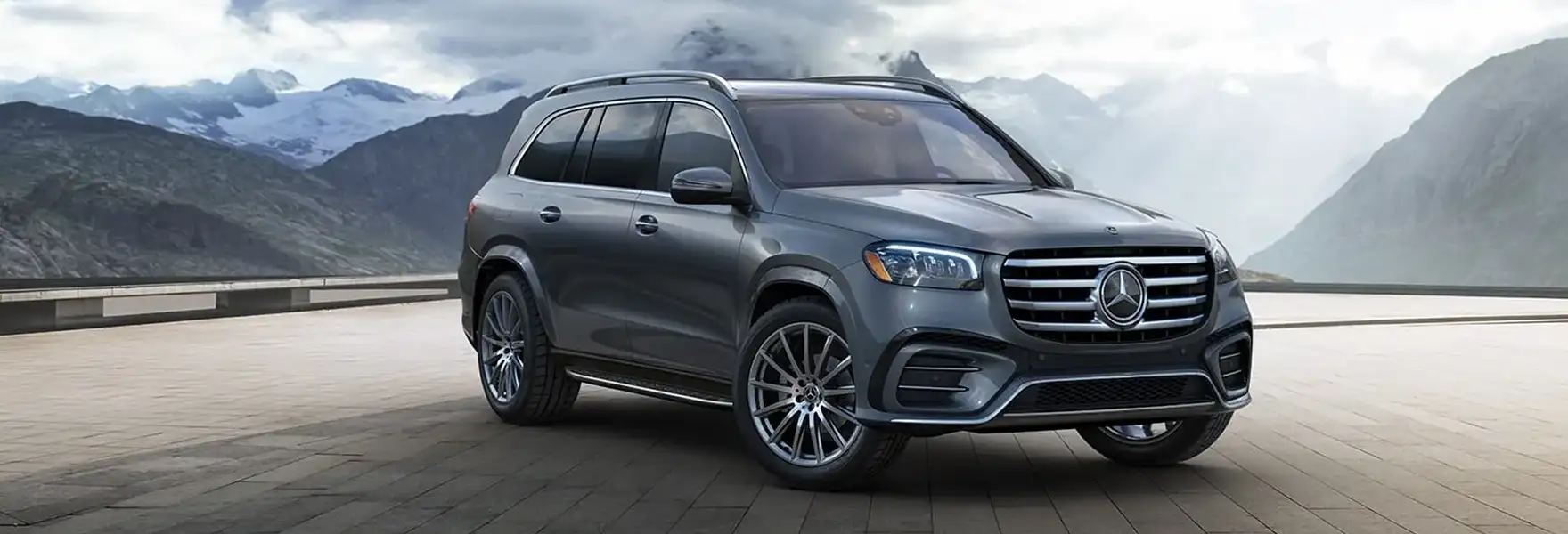 Dark gray Mercedes-Benz GLS SUV on a mountain highway with snow-capped peaks behind