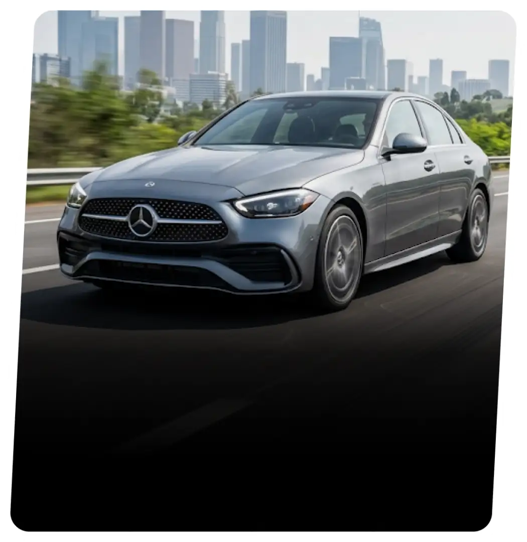 Gray Mercedes-Benz sedan on a highway with a city skyline behind it