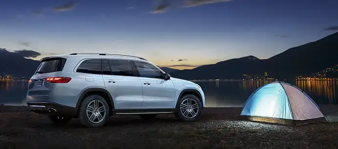 Light blue Mercedes-Benz GLS parked at dusk beside a lit tent on a lakeshore