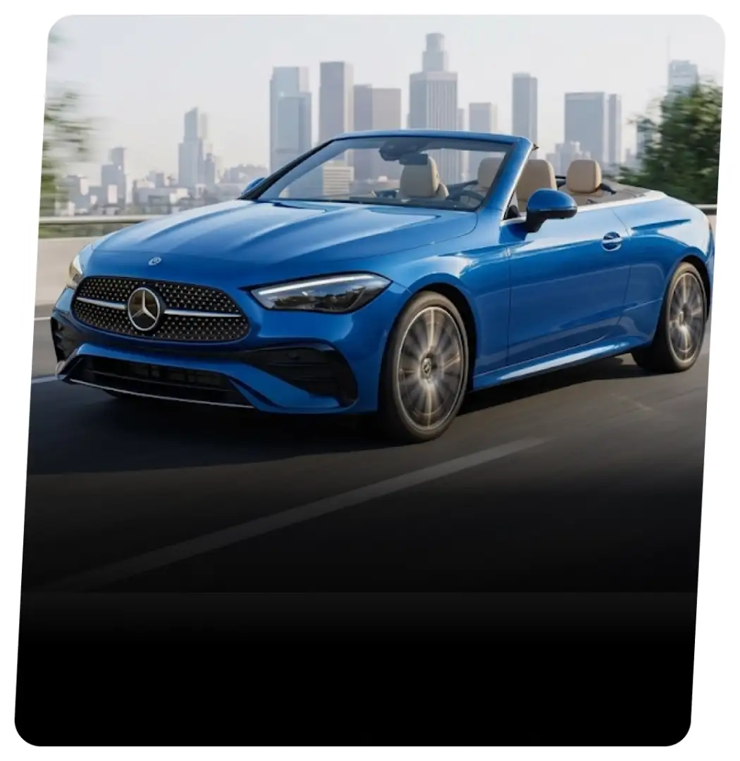 Blue Mercedes-Benz convertible with the top down on a highway near a city skyline