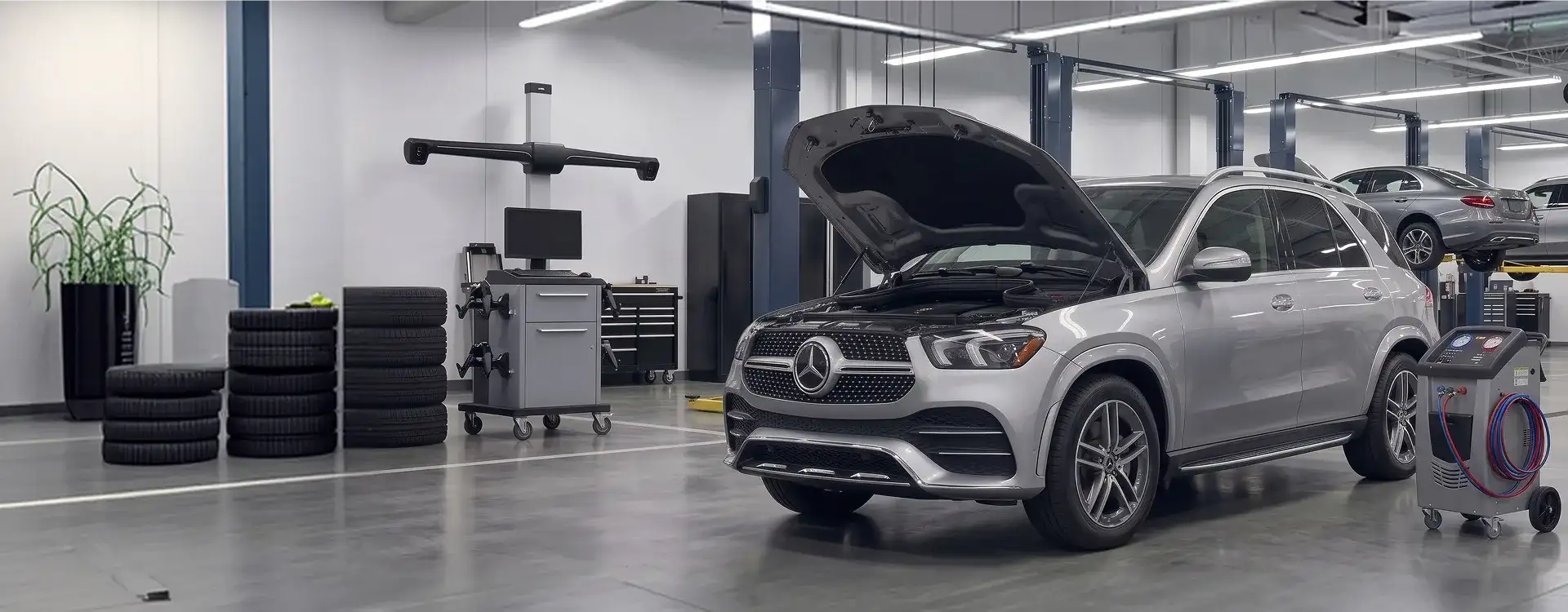 Silver Mercedes-Benz GLE SUV with its hood raised beside an air conditioning recovery machine in the Helms Bros service shop