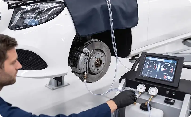 Technician performing a brake fluid exchange on a white Mercedes-Benz sedan using a digital brake fluid service machine