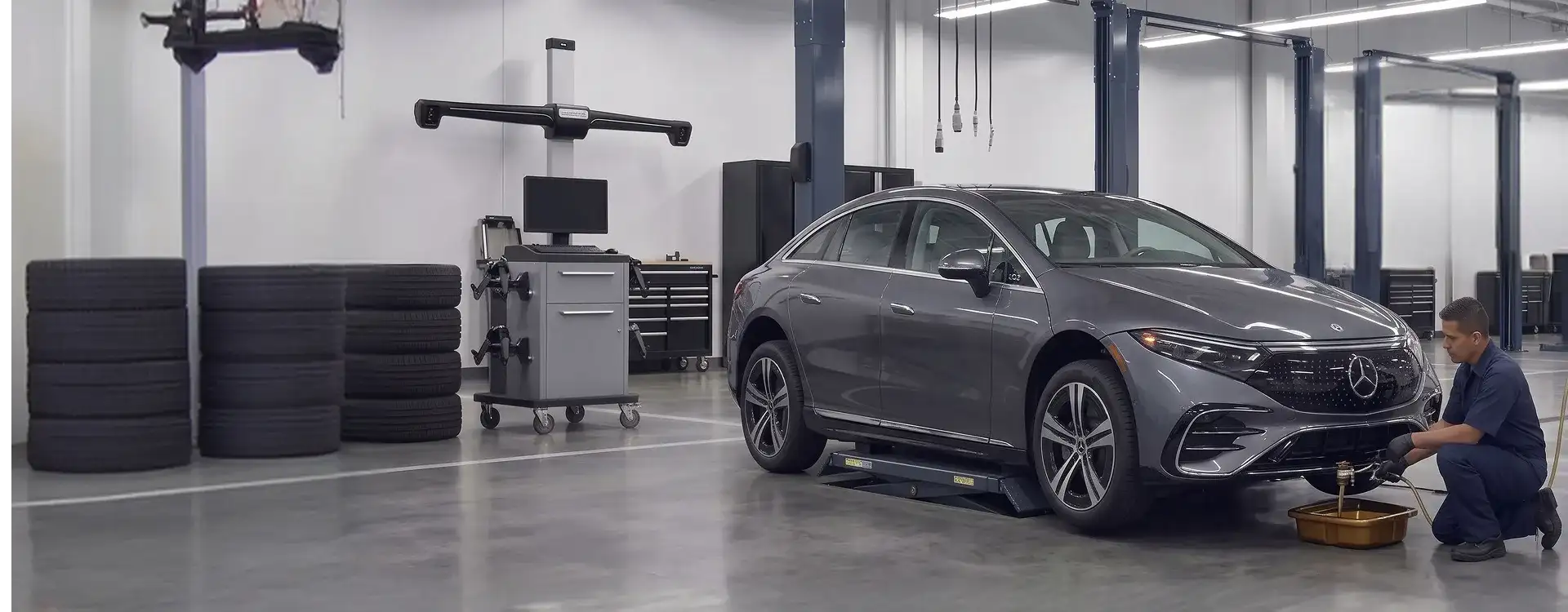 Grey Mercedes-Benz EQS sedan on a service rack while a technician drains fluid into a pan beside a Mercedes-Benz fluid exchange machine