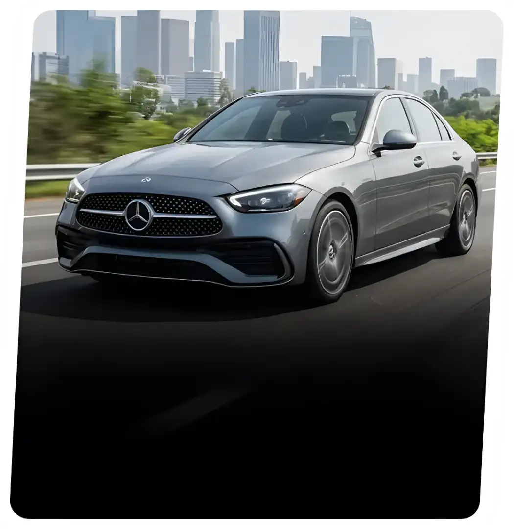 Silver Mercedes-Benz sedan driving on a highway with a city skyline behind it.