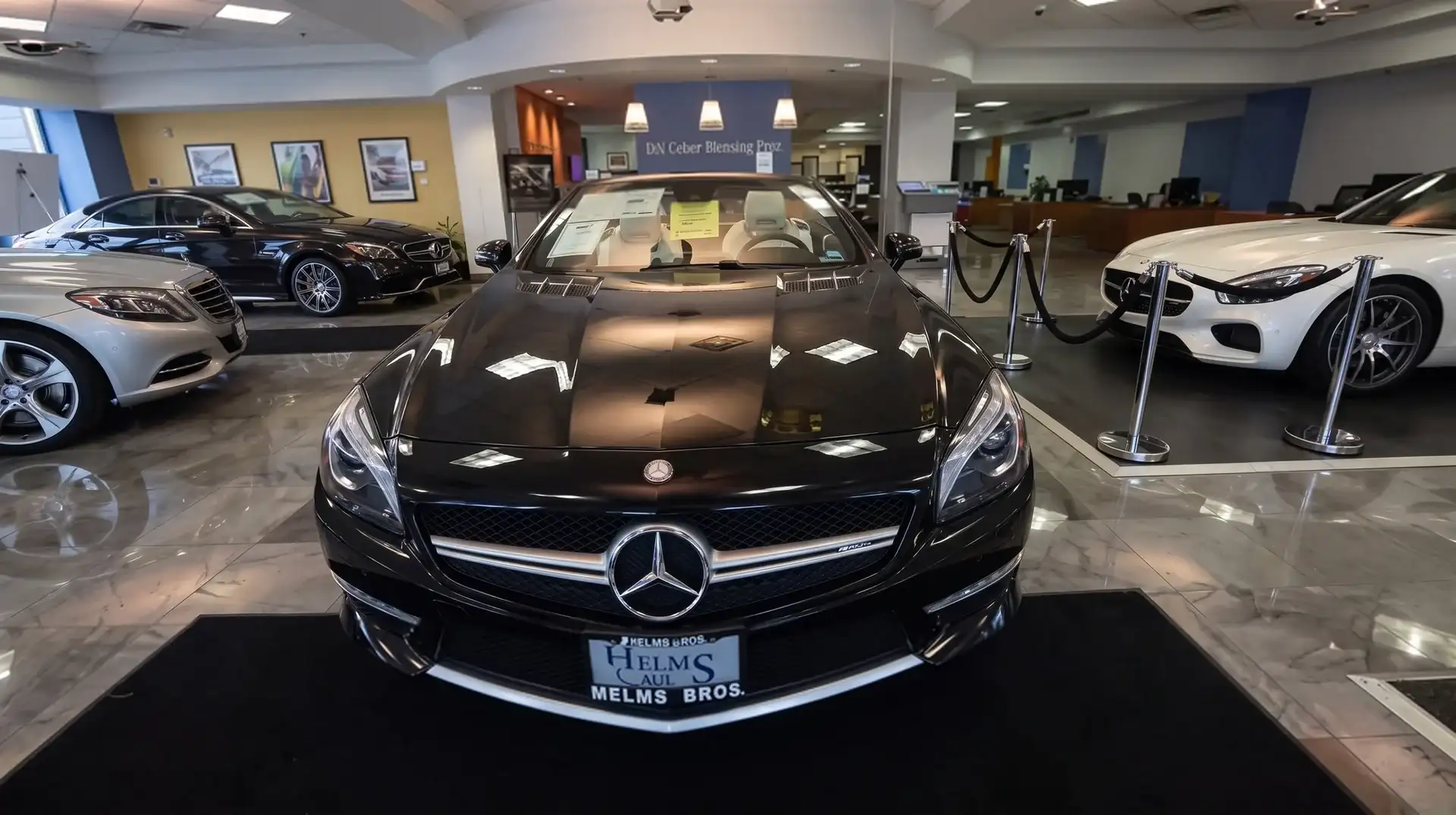 Mercedes-Benz cars on a showroom floor, a black roadster in the foreground between a sedan and a white coupe