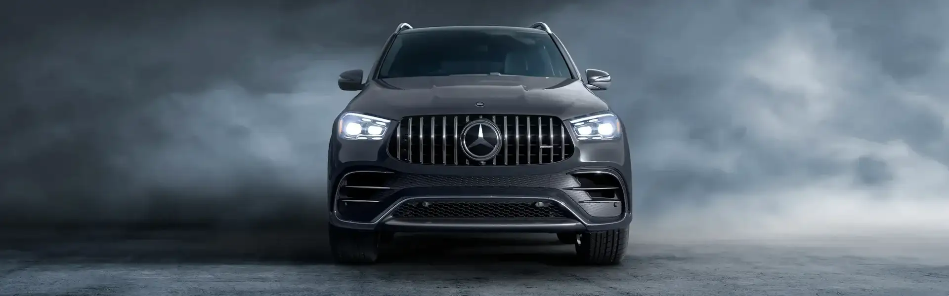 A dark Mercedes-AMG GLE SUV seen head-on in a studio haze, headlights lit