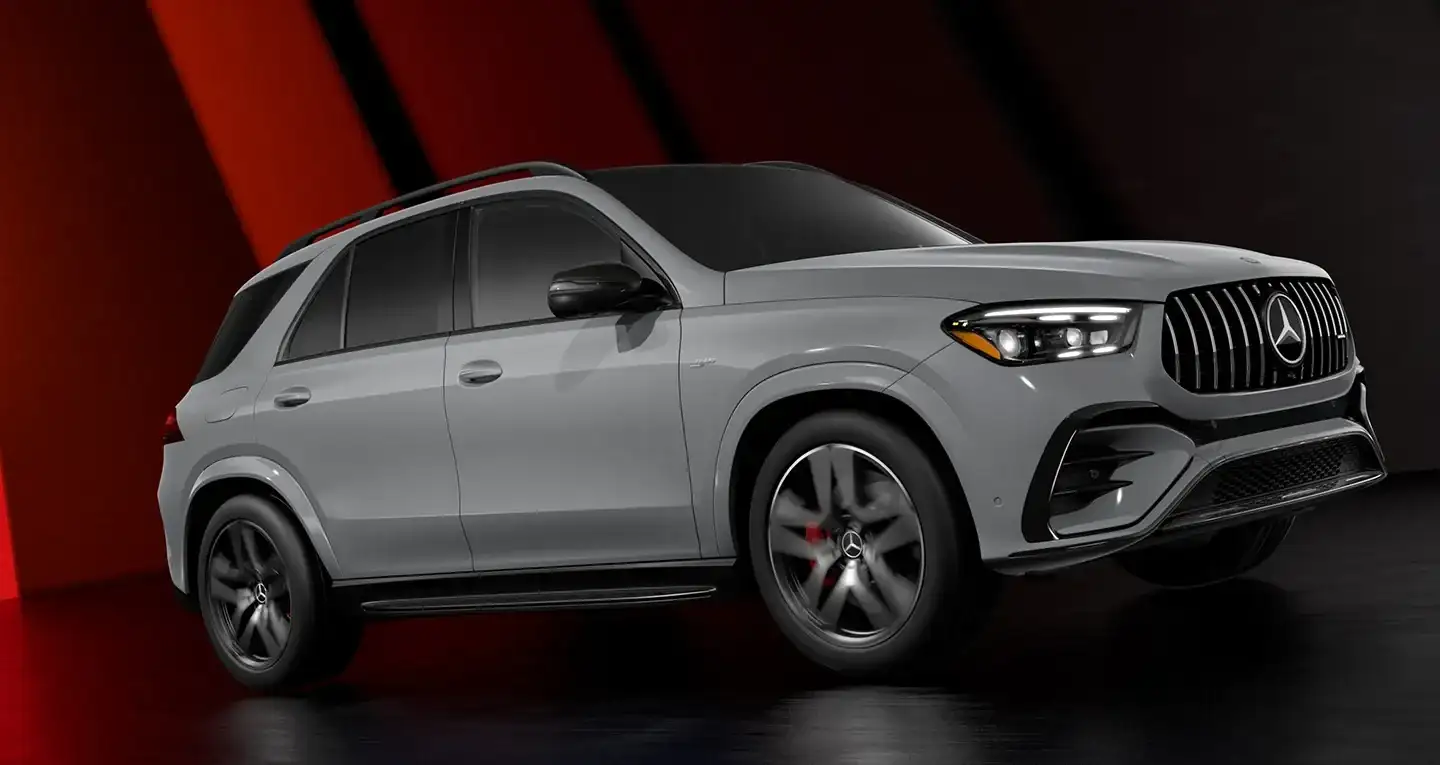 A grey Mercedes-AMG GLE SUV in a dark studio against red panels, front three-quarter view