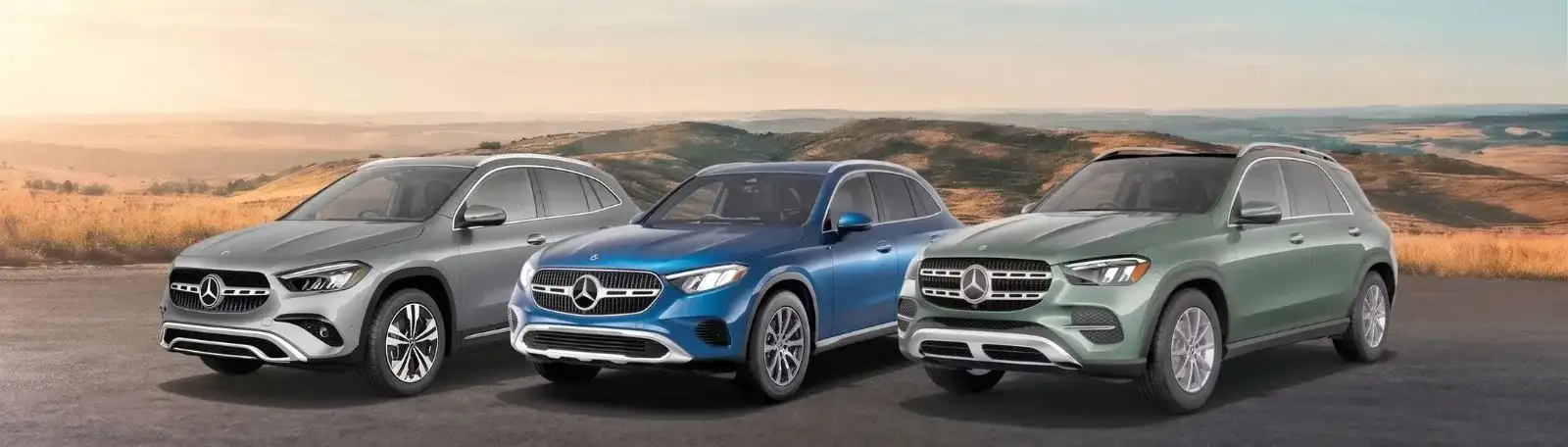 Three Mercedes-Benz SUVs lined up on a hilltop at sunrise, in silver, blue and green