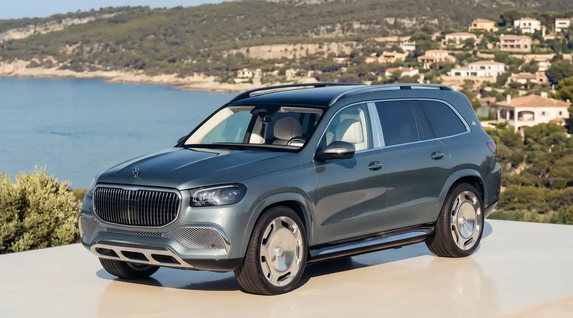 A pale green Mercedes-Benz SUV parked on a terrace above a coastal bay, front three-quarter view