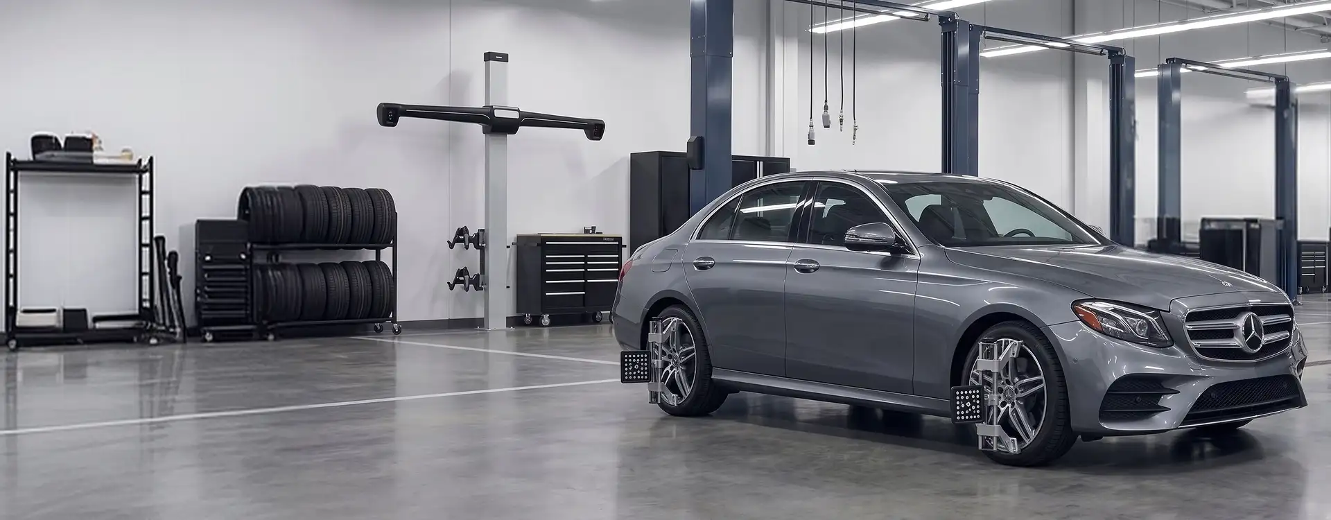 Grey Mercedes-Benz E-Class on the Helms Bros alignment rack with wheel target clamps fitted and the alignment tower behind