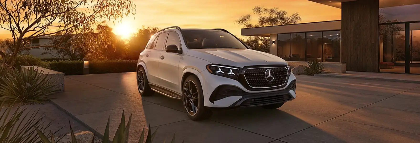 White Mercedes-Benz GLE SUV on a driveway beside a modern house at sunset