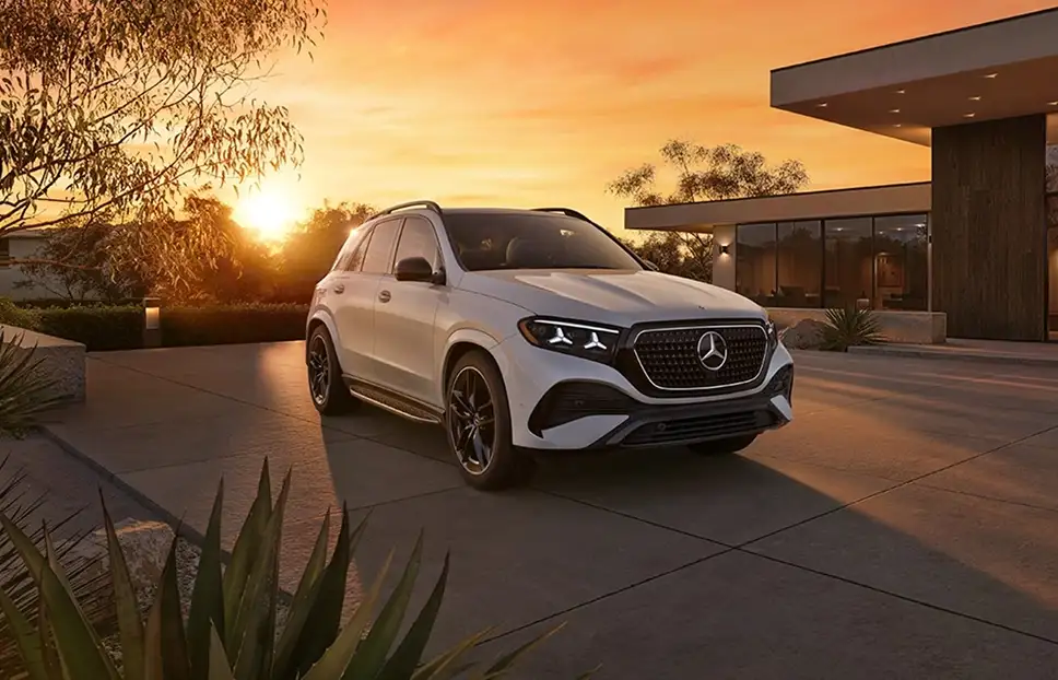White Mercedes-Benz GLE SUV on a driveway beside a modern house at sunset