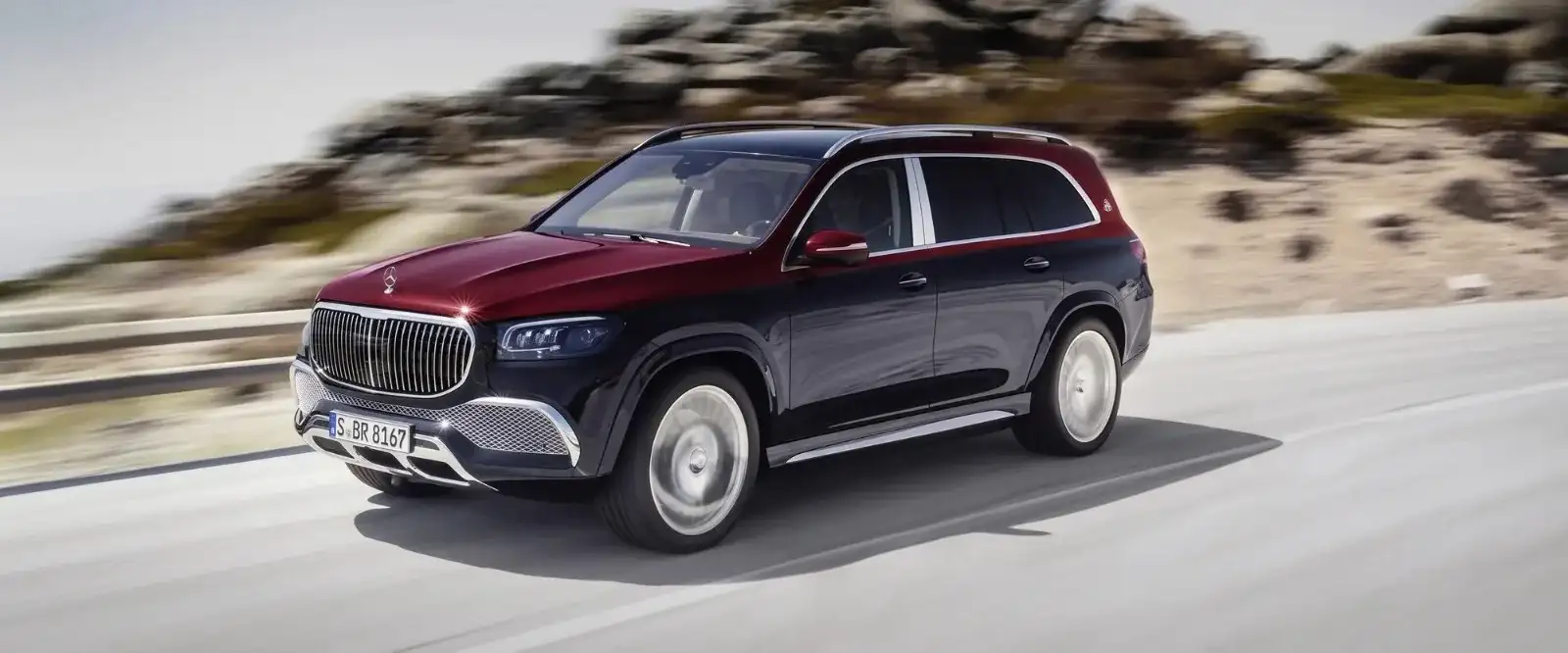 A two-tone red and black Mercedes-Benz SUV driving a coastal road, front three-quarter view