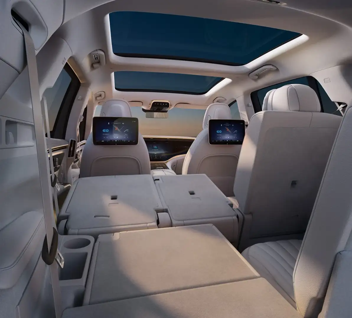 The rear cabin of a Mercedes-Benz EQS SUV in cream leather, two rear-seat screens lit and the panoramic roof above
