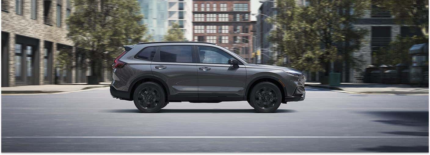 Side profile of a grey 2026 Honda CR-V driving on a city street.