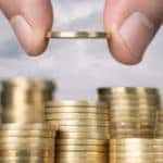 A hand dropping a coin into a pile of money