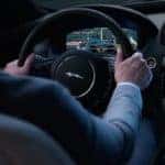Shot of driver with hands on wheel and touchscreen in dash
