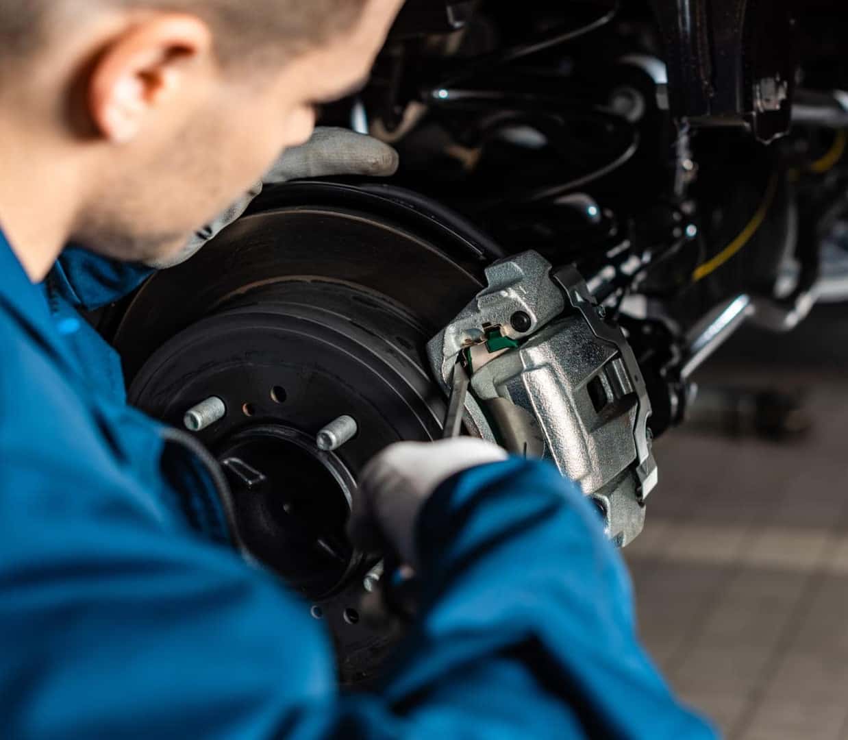 A mechanic in blue overalls is inspecting a car's brake system.