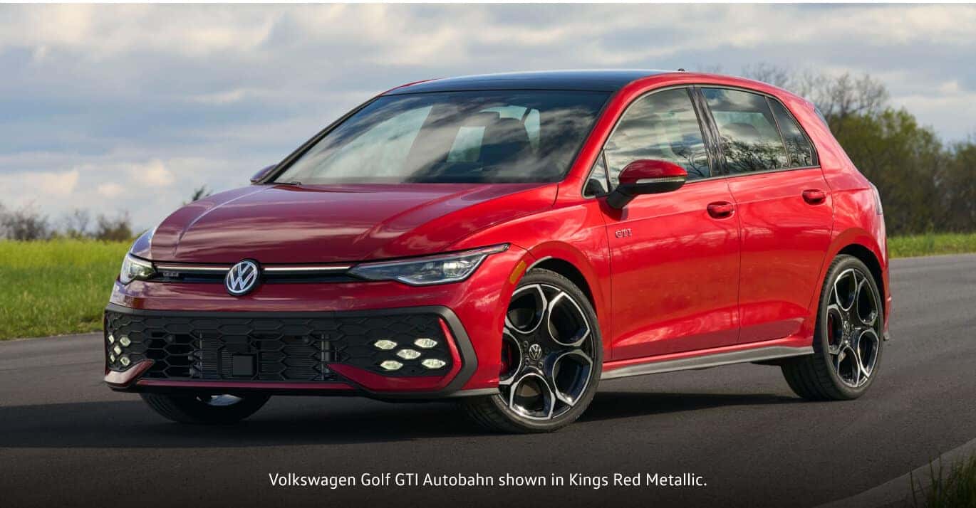 2026 Volkswagen Kings Red Metallic Volkswagen Golf GTI Autobahn parked on a paved road with trees in the background.