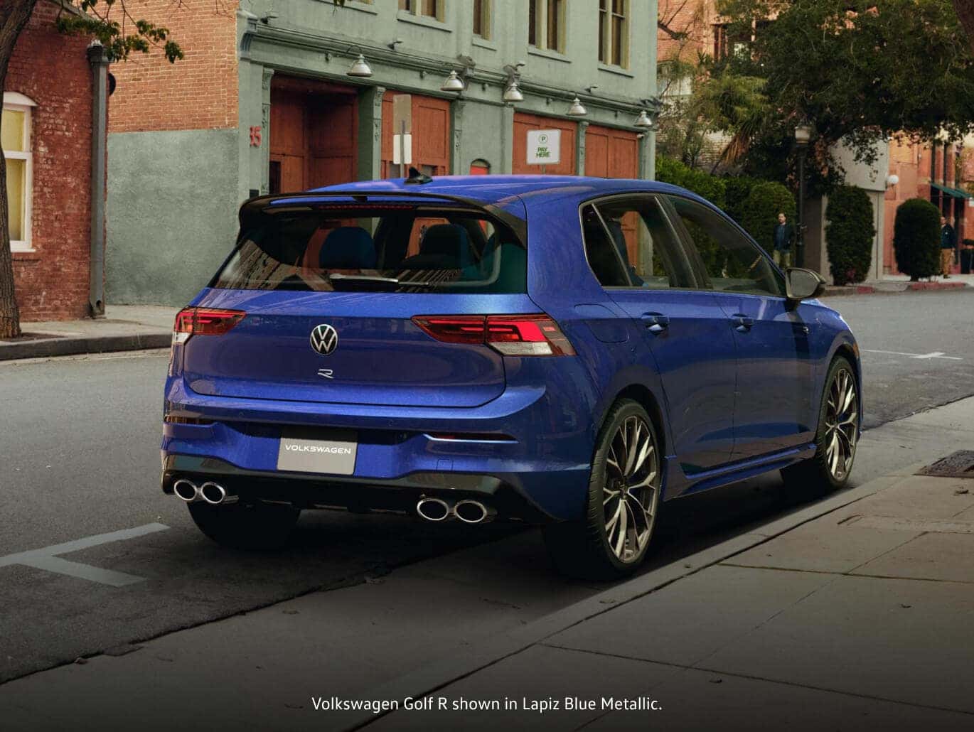 2026 Volkswagen Lapiz Blue Metallic Golf R hatchback parked on a city street as a person walks past.