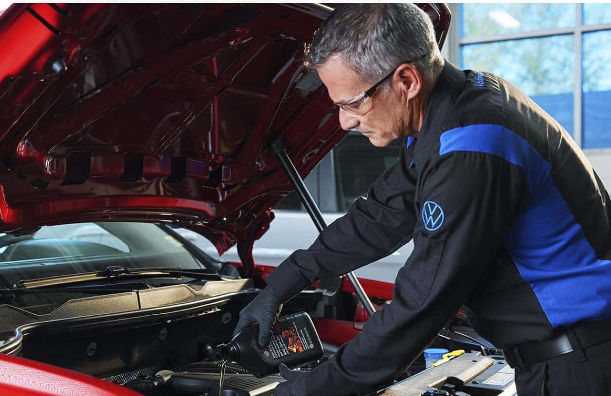 A VW Service Technician pours oil into a VW vehicle inside a service center.