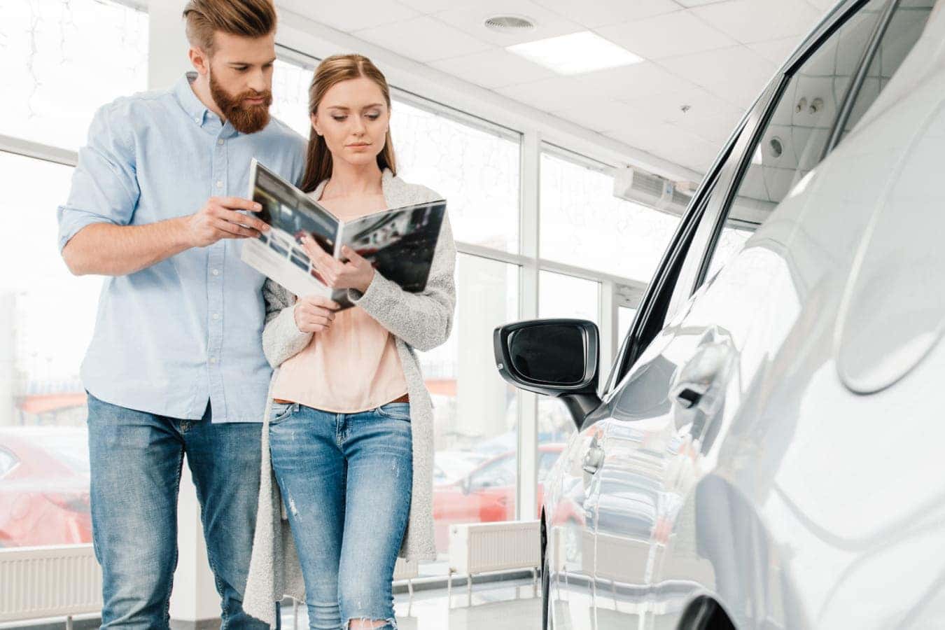 Couple reviewing vehicle information while browsing a car inside a dealership showroom.