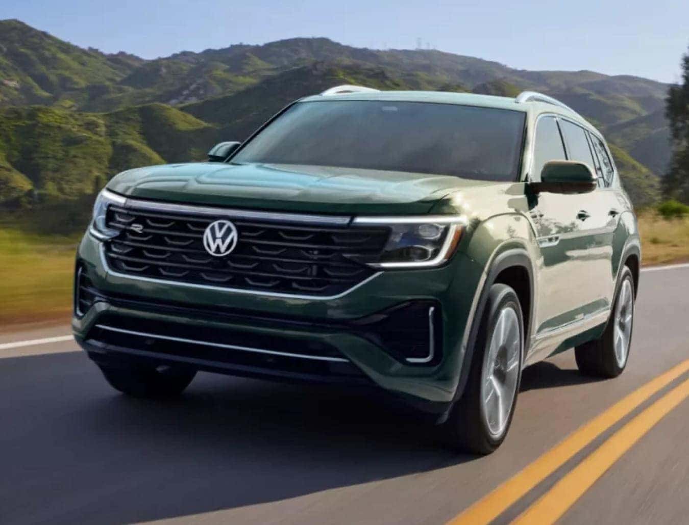 Green Volkswagen SUV driving on a winding road with mountains in the background.