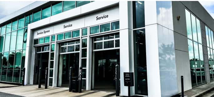 Exterior view of a Volkswagen dealership's service center, featuring multiple glass garage doors, designated Service Xpress and Service entrances, and a modern glass-paneled facade.