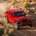 Red Jeep Gladiator descending gravel road on mountain
