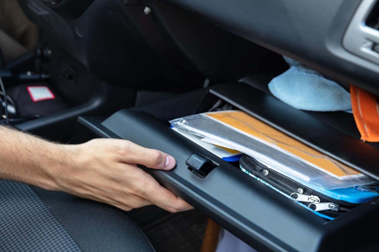 A caucasian hand opening an organized glove box in a car. 