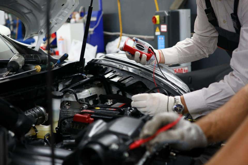 Two hands fixing a vehicle under the hood. 