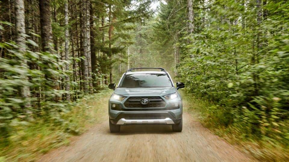 Front view of a blue gray 2020 RAV4 driving through the woods