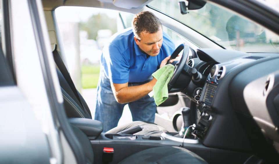 A man scrubbing his steering wheel with a microfiber cloth