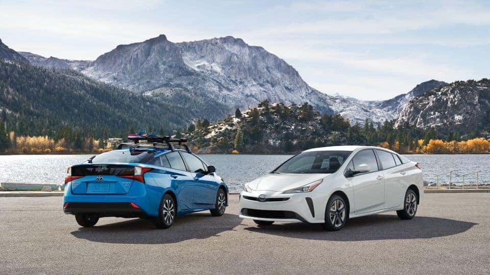 A Blue and a White 2021 Toyota Prius against a mountain and lake. 