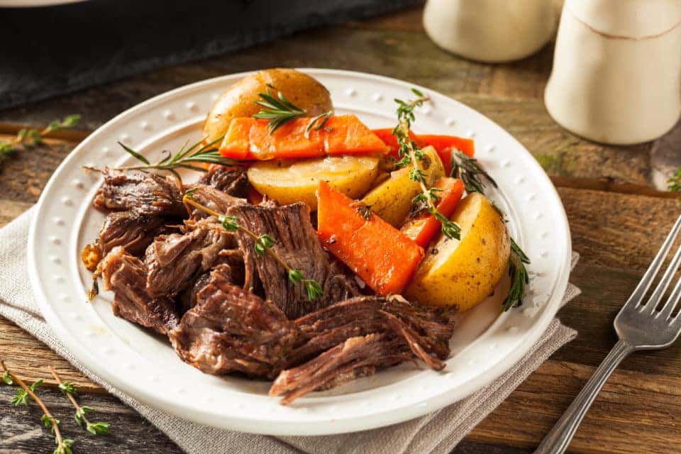 homemade pot roast with carrots and potatoes in a white bowl.