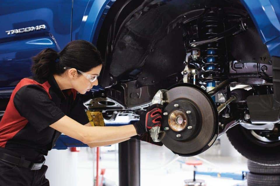 A Toyota service technician doing brake work on a blue Toyota Tacoma truck